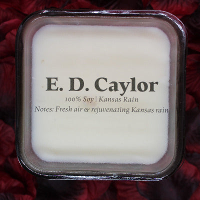 E. D. Caylor Kansas rain soy candle with lid on it sitting on a bed of rose petals
