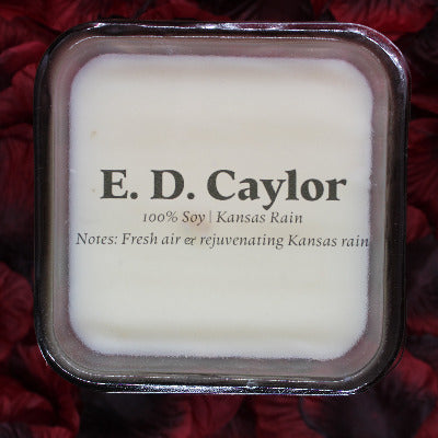 E. D. Caylor Kansas rain soy candle with lid on it sitting on a bed of rose petals