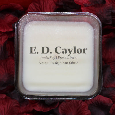 E. D. Caylor fresh linen soy candle with lid on it sitting on a bed of rose petals