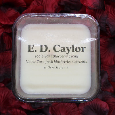 E. D. Caylor blueberry cream soy candle with lid on it sitting on a bed of rose petals