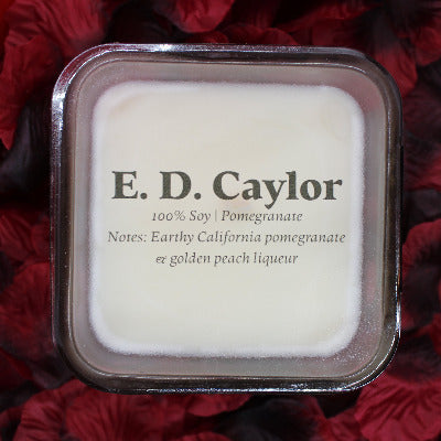 E. D. Caylor pomegranate soy candle with lid on it sitting on a bed of rose petals