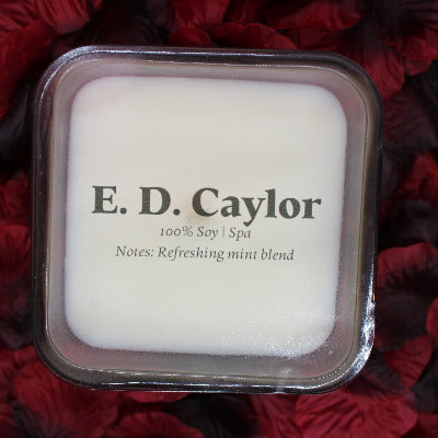 E. D. Caylor spa soy candle with lid on it sitting on a bed of rose petals